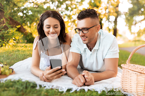 Image of happy couple with smartphone at picnic in park