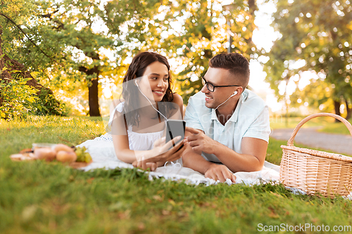 Image of couple with earphones and smartphone at picnic