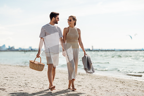 Image of happy couple with picnic basket walking on beach