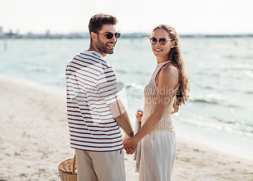 Image of happy couple with picnic basket walking on beach