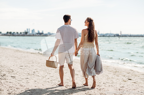 Image of happy couple with picnic basket walking on beach