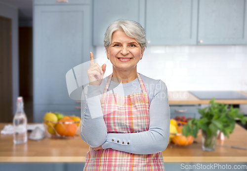 Image of smiling senior woman in apron pointing finger up