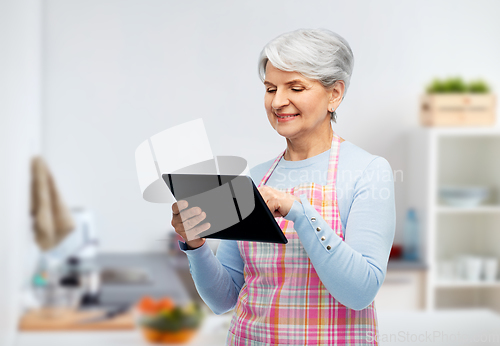 Image of old senior woman in kitchen apron with tablet pc