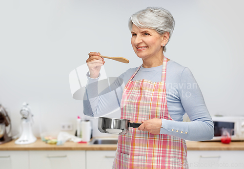 Image of senior woman in apron with pot cooking food