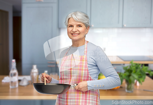 Image of smiling senior woman in apron with frying pan