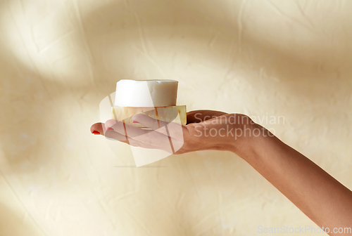 Image of hand holding bar of craft soap on beige background