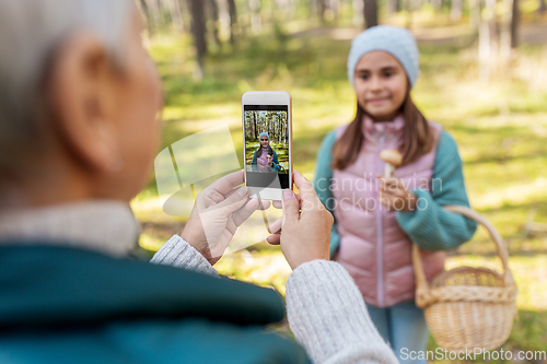 Image of grandma photographing granddaughter with mushrooms