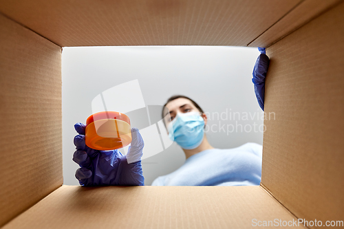 Image of woman in mask unpacking parcel box with cosmetics