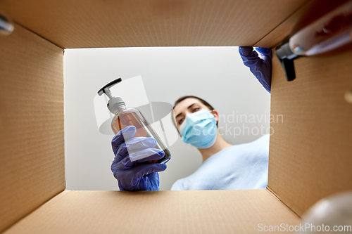 Image of woman in mask unpacking parcel box with cosmetics