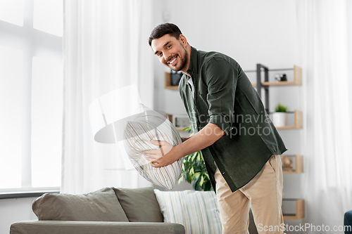 Image of happy smiling man arranging sofa cushions at home