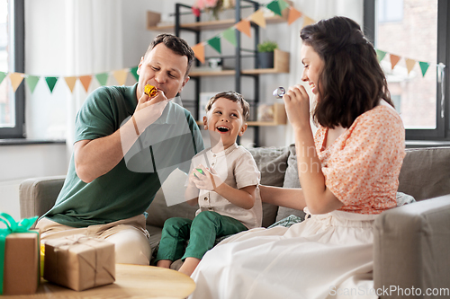 Image of happy family with gifts and party blowers at home