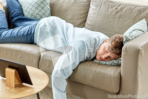 Image of bored man with tablet pc lying on sofa at home