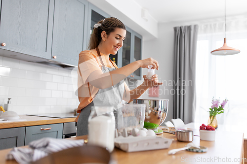 Image of happy young woman cooking food on kitchen at home