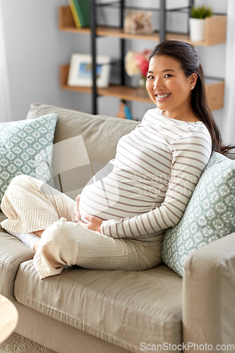 Image of happy pregnant asian woman sitting on sofa at home
