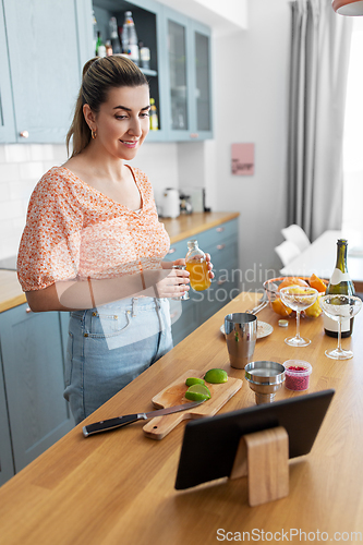 Image of woman with tablet pc making cocktails at kitchen
