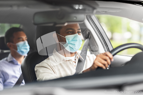 Image of male driver in mask driving car with passenger