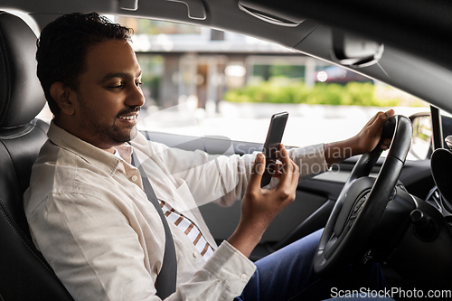 Image of smiling indian man in car using smartphone