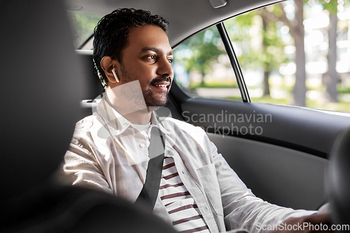 Image of indian male passenger with earphones in taxi car