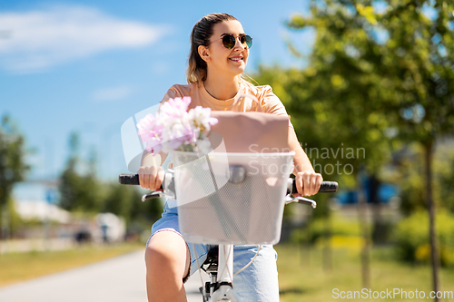 Image of woman with flowers in bicycle basket in city