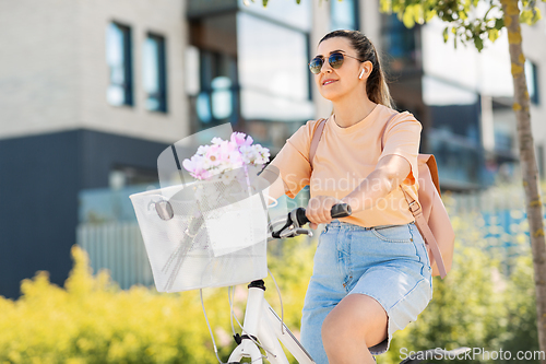 Image of happy woman with earphones riding bicycle in city