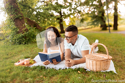 Image of happy couple reading book on picnic at summer park