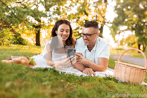 Image of couple with earphones and smartphone at picnic
