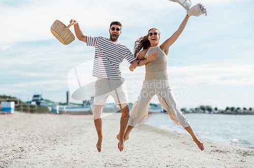 Image of happy couple with picnic basket jumping on beach