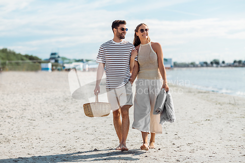 Image of happy couple with picnic basket walking on beach