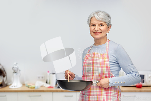 Image of smiling senior woman in apron with frying pan