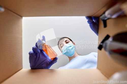 Image of woman in mask unpacking parcel box with cosmetics