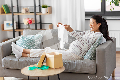 Image of happy pregnant woman with baby's bodysuit at home