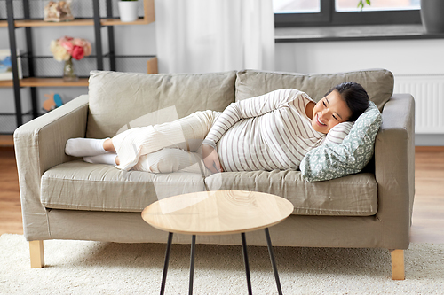 Image of happy pregnant asian woman lying on sofa at home