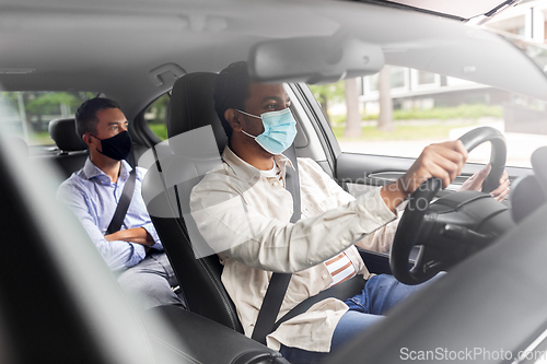 Image of male driver in mask driving car with passenger