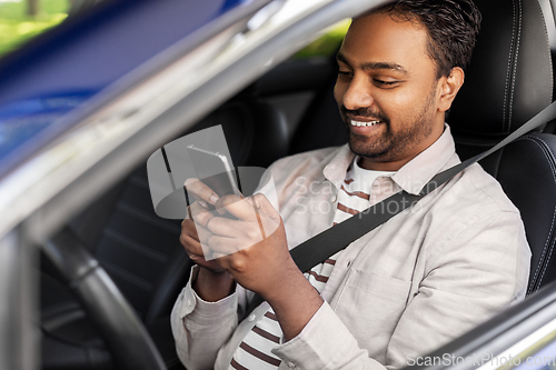 Image of smiling indian man in car using smartphone