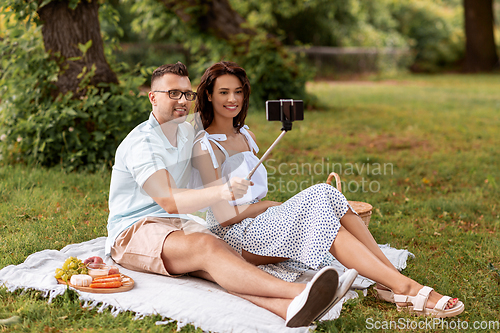 Image of happy couple taking selfie at picnic in park