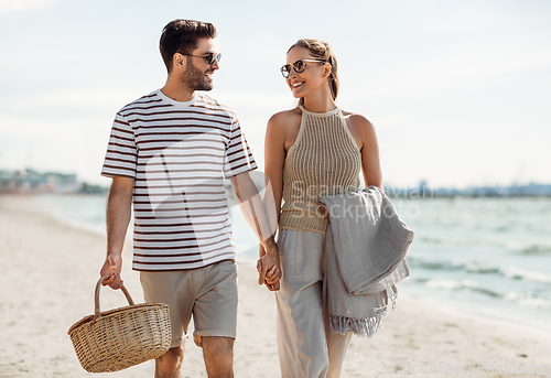 Image of happy couple with picnic basket walking on beach
