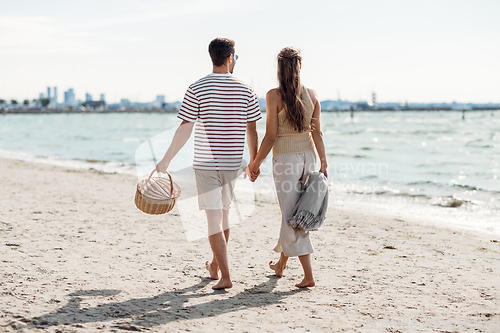 Image of happy couple with picnic basket walking on beach