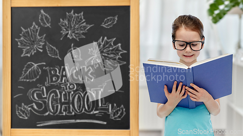 Image of little student girl in eyeglasses reading book