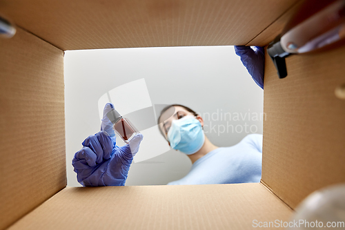 Image of woman in mask unpacking parcel box with cosmetics