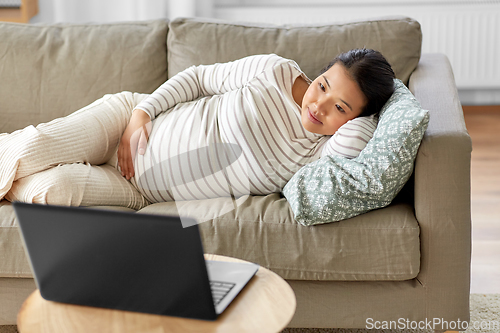 Image of happy pregnant asian woman with laptop at home