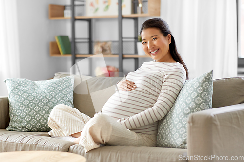 Image of happy pregnant asian woman sitting on sofa at home