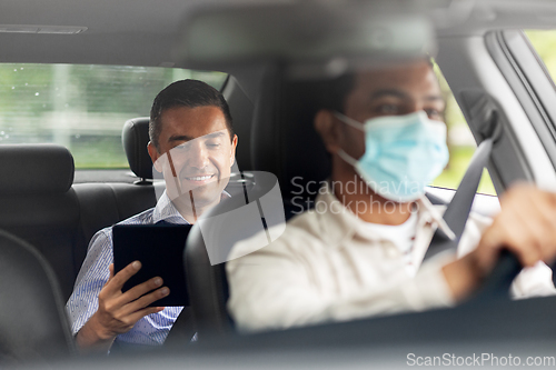 Image of passenger with tablet pc and car driver in mask