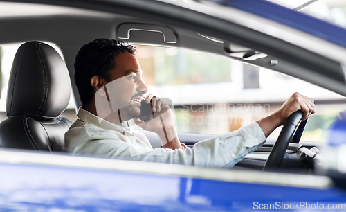 Image of indian man driving car and calling on smartphone