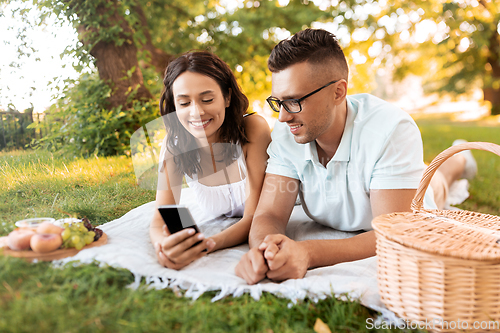 Image of happy couple with smartphone at picnic in park