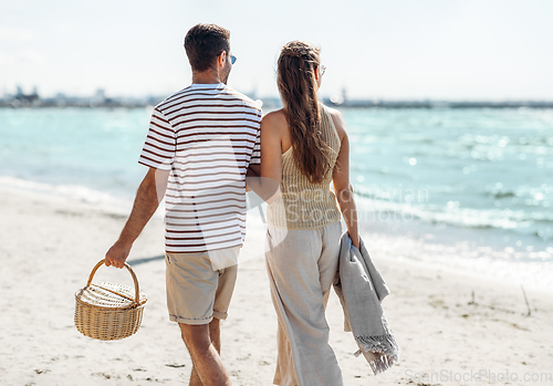 Image of happy couple with picnic basket walking on beach