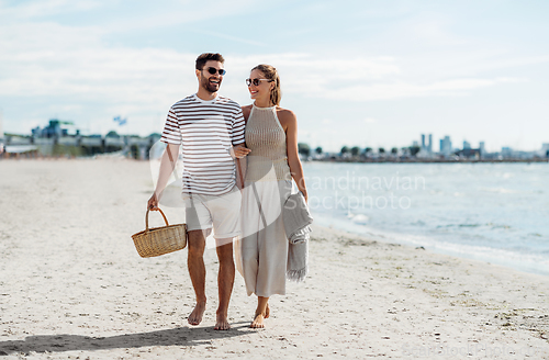 Image of happy couple with picnic basket walking on beach