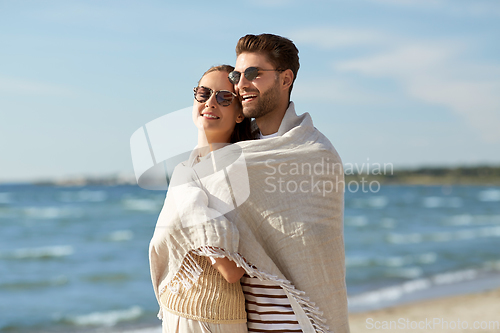 Image of happy couple covered with blanket hugging on beach