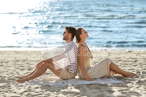 Image of happy couple sitting back to back on summer beach