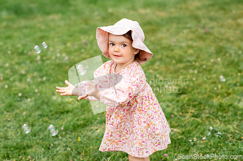 Image of happy baby girl playing with soap bubbles outdoors