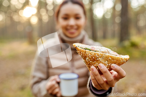 Image of woman drinking tea with sandwich in autumn forest